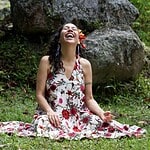 Woman meditating outdoors in a floral dress with a joyful expression.