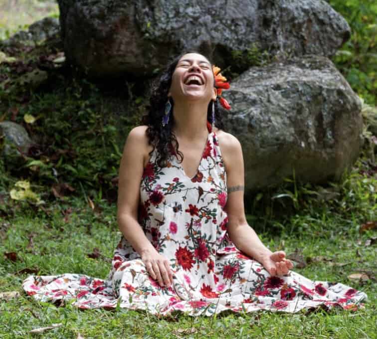 Woman meditating outdoors in a floral dress with a joyful expression.