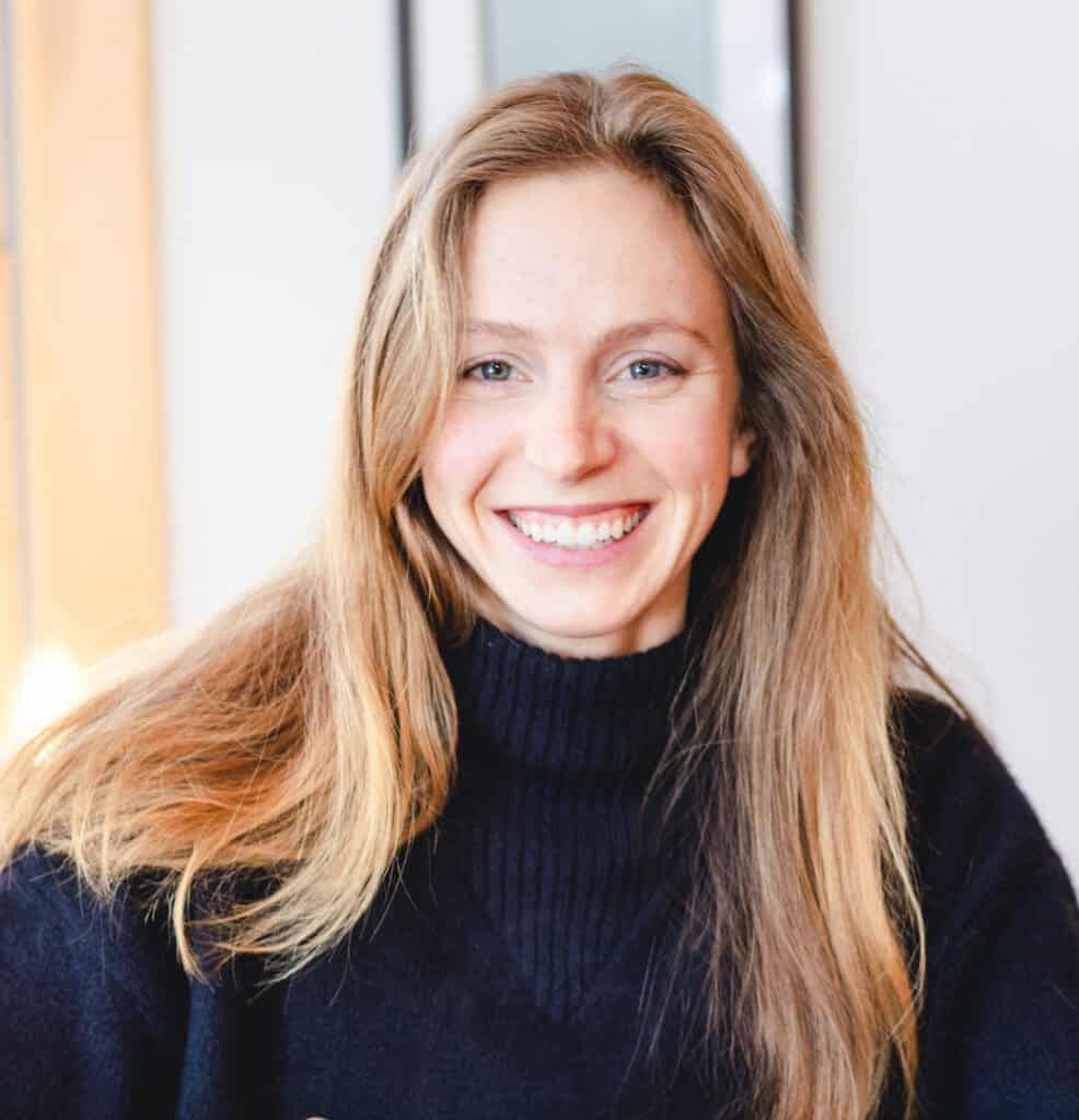 Smiling woman with long blonde hair in dark sweater, natural light.