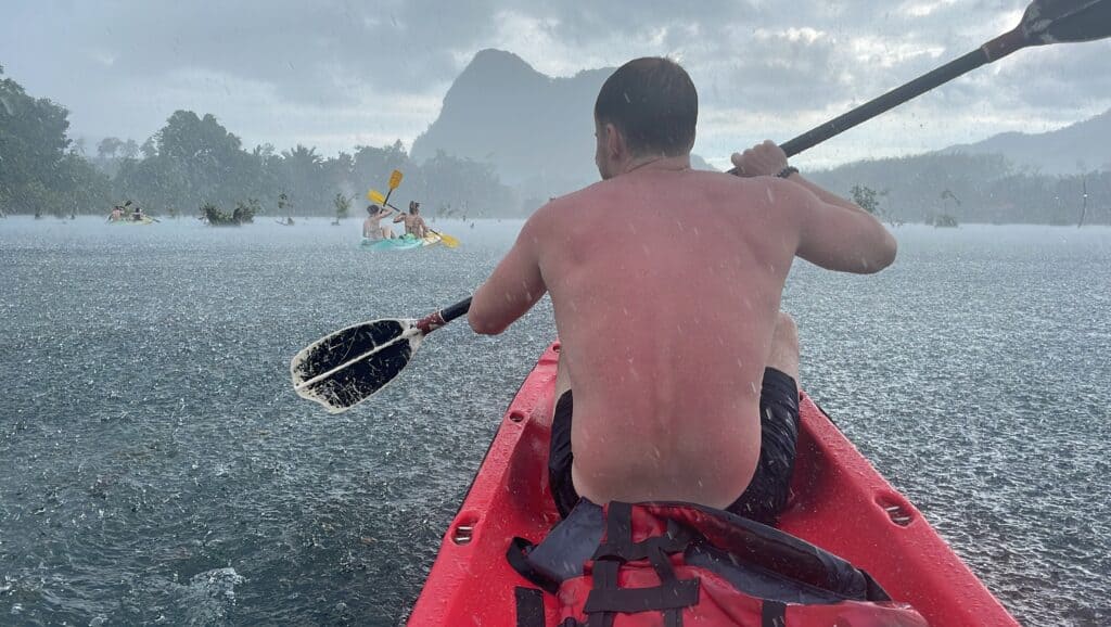Kayaker paddling a red boat on a lake with distant mountains and cloudy sky.