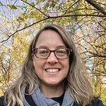 Portrait of a smiling woman with glasses outdoors among autumn trees, representing the Global Ecov­­.