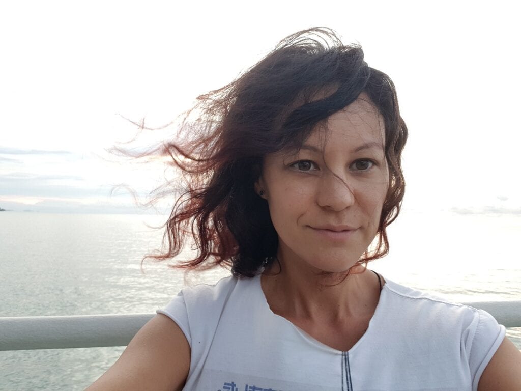 Woman taking a selfie with ocean background and wind-blown hair.