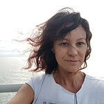 Woman taking a selfie with ocean background and wind-blown hair.