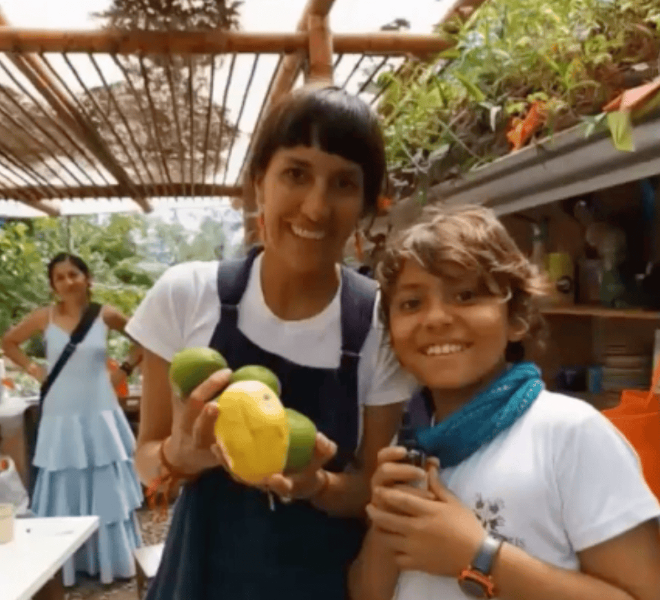 Two youths smiling and holding fresh fruits in a community garden.
