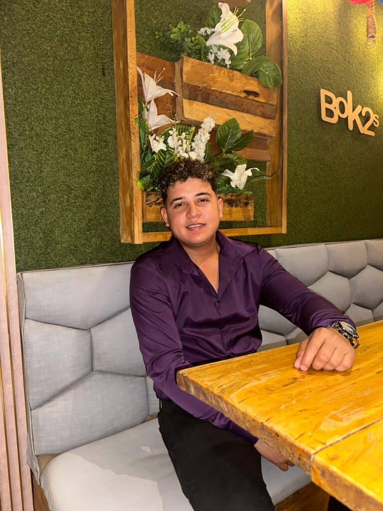 Person seated at wooden table in cozy eco-friendly venue with greenery backdrop.