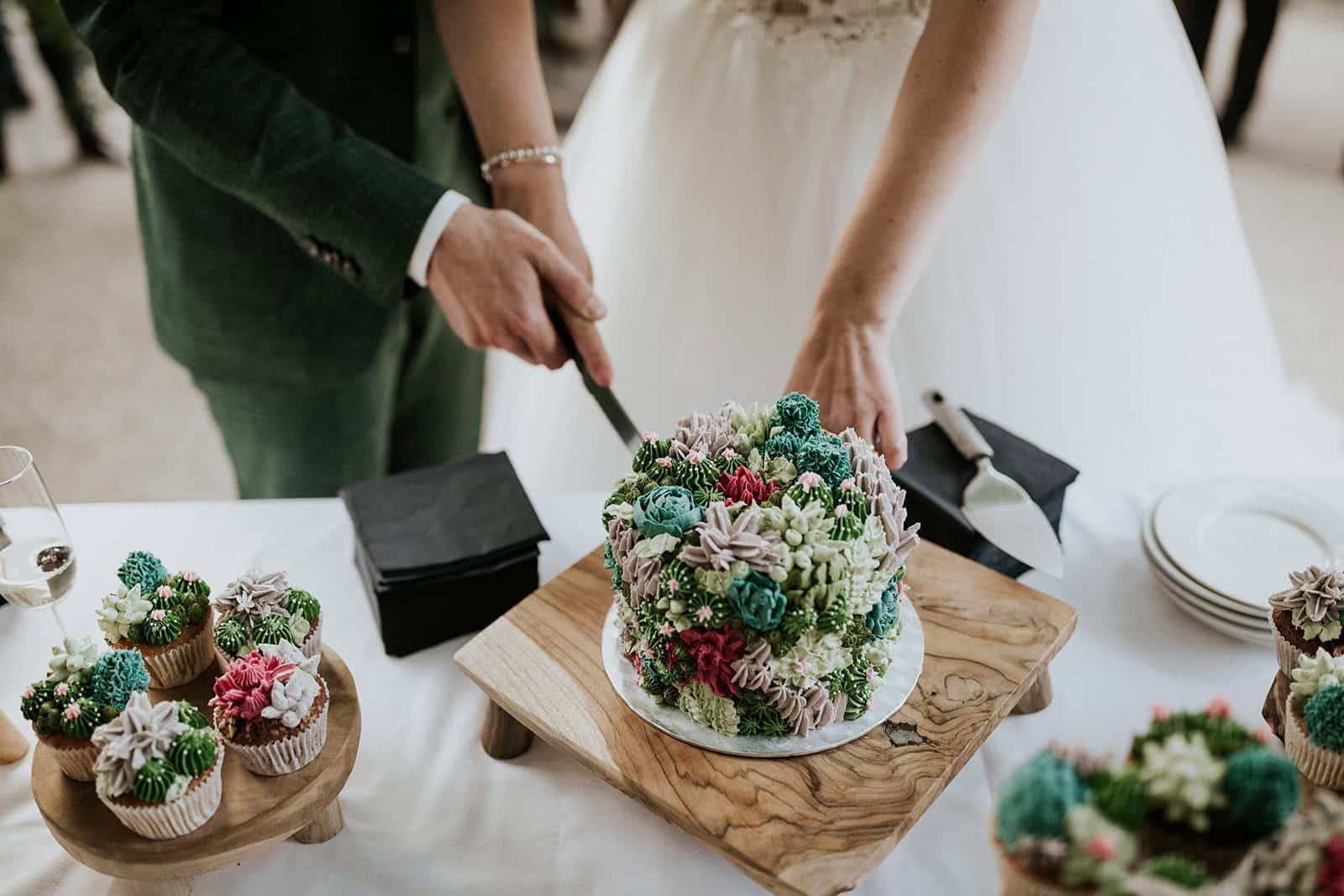 Op de foto staat een bruidspaar dat een bruidstaart aan het aansnijden is. Een bruidstaart kiezen doe je bij Amsterdam Cupcake Company!