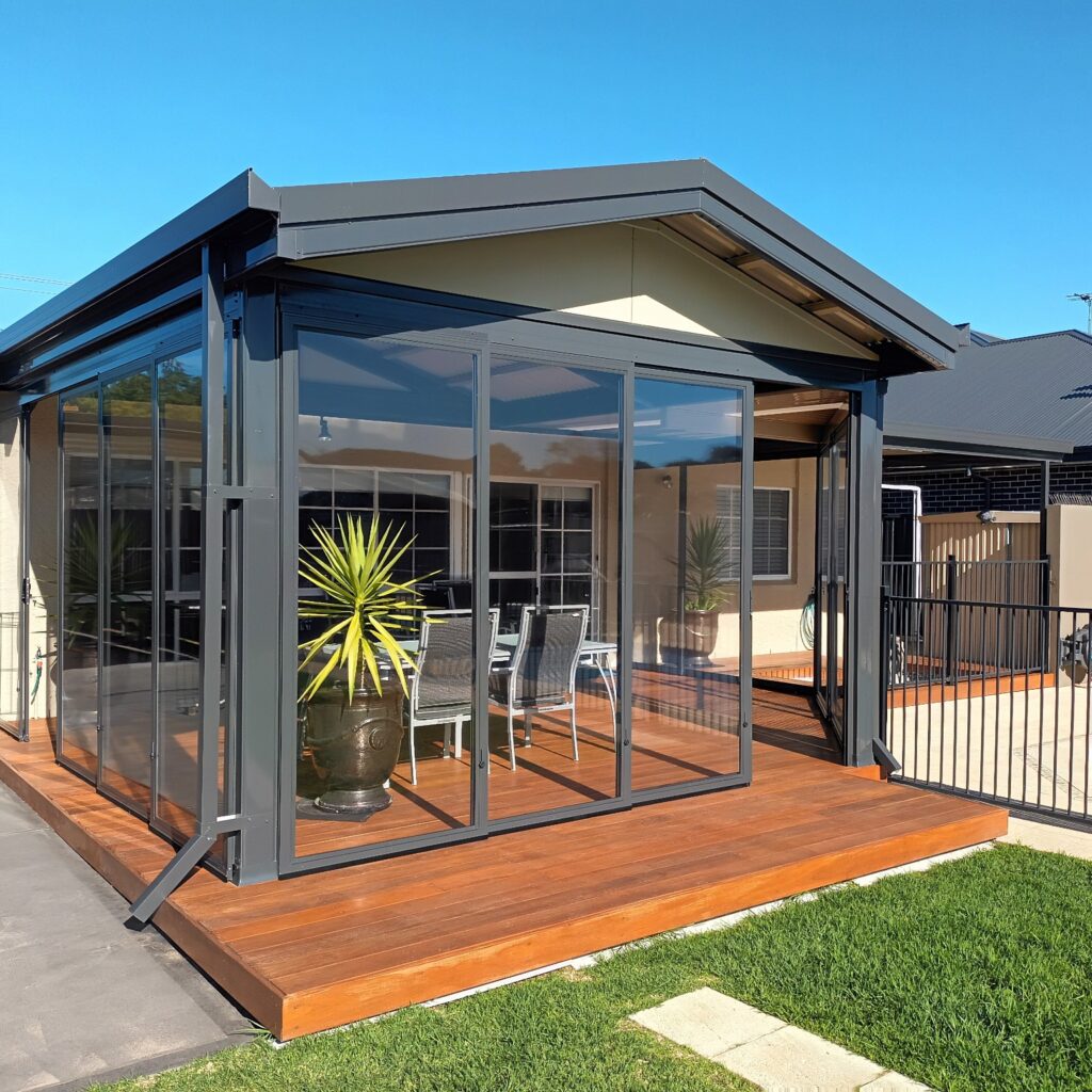 Modern outdoor weather screen enclosure with glass walls and wooden deck.