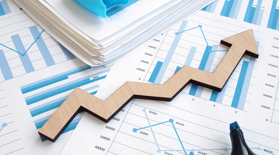 A wooden arrow pointing upward over a pile of financial charts and papers, symbolizing business growth consulting and strategic financial planning.