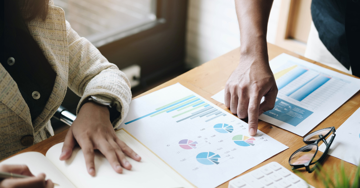 Two professionals reviewing financial charts and graphs on a table, representing financial analysis for businesses and profitability consulting.