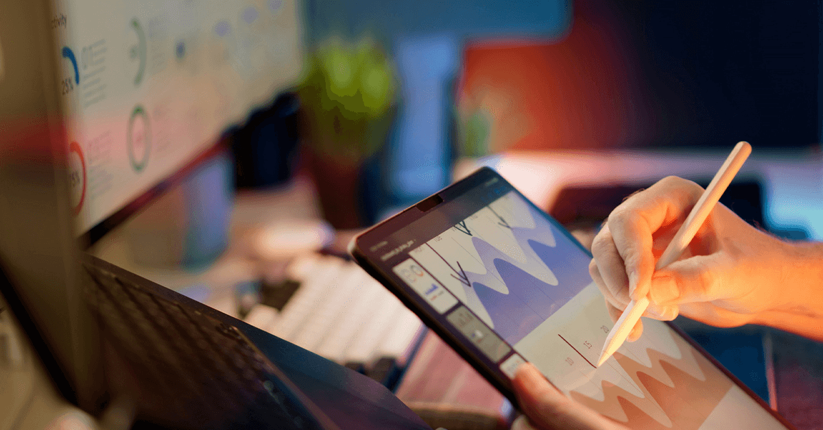 A person's hand using a stylus on a digital tablet displaying financial waveforms and data charts, symbolizing KPI analysis and strategic financial planning.