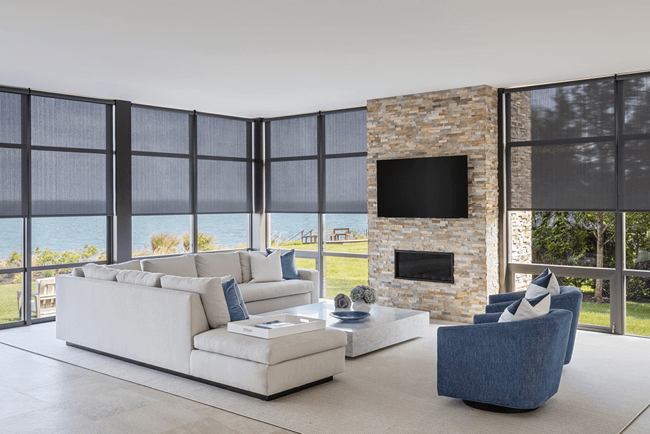 Modern living room with dark solar shades on large windows overlooking a lake.