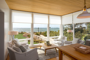 Bright living room with white roller shades on large windows showcasing an ocean view.