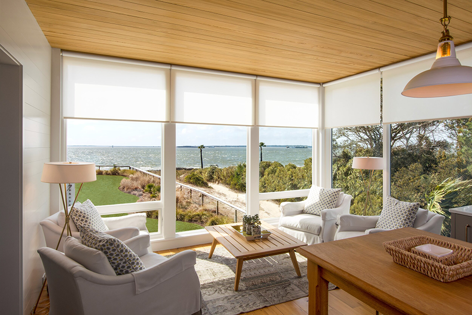 Bright living room with white roller shades on large windows showcasing an ocean view.
