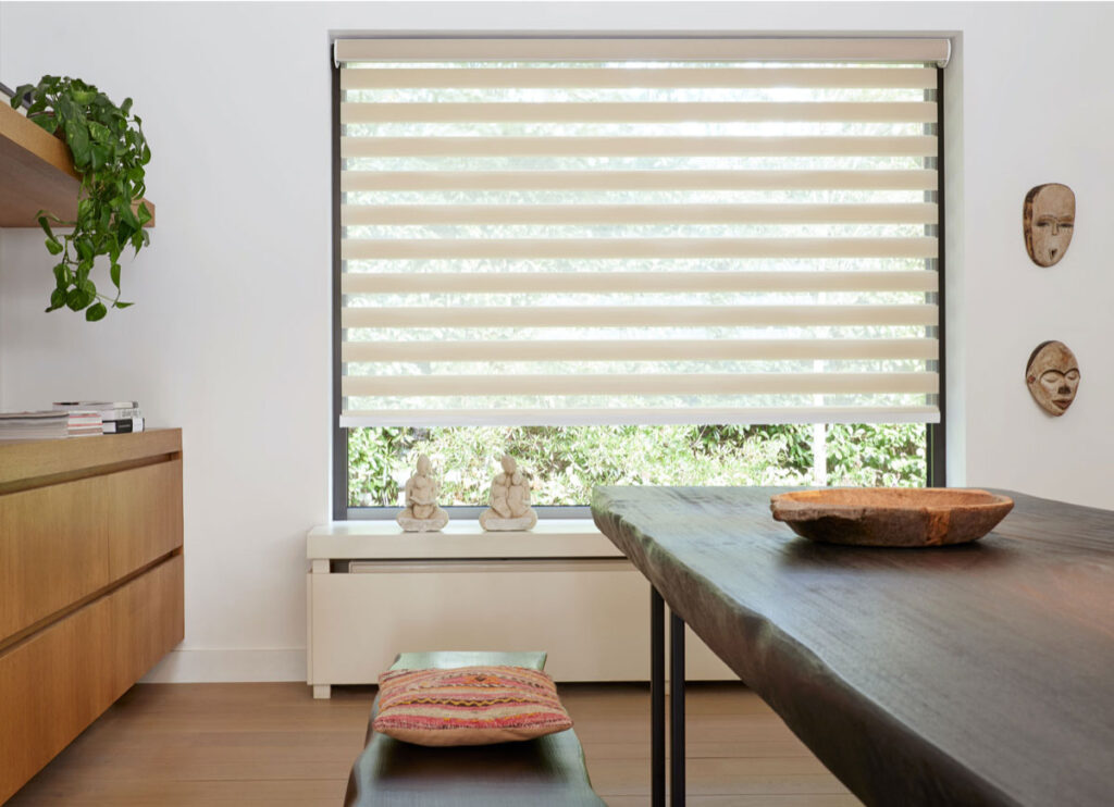 roller shades on a window with a table on it and masks hanging on the wall