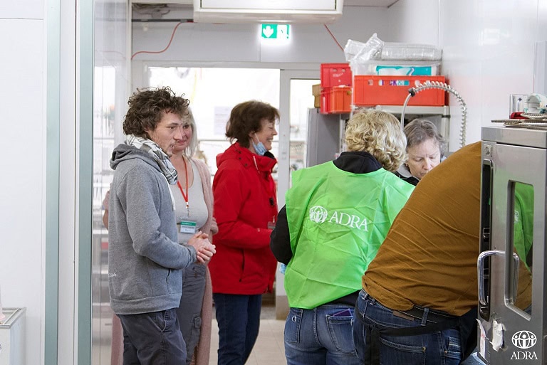 1. Mehrere Menschen in einem Supermarkt oder Lager, einige tragen ADRA- und ADVENT-Verlag-Workshops, mit Blick auf eine Verkaufs- oder Verteilstation.