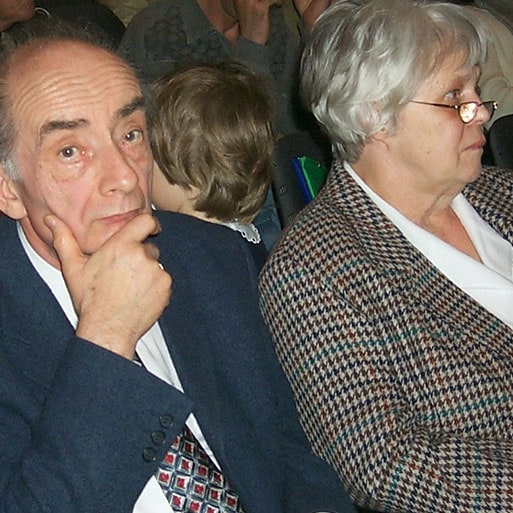 Ein älterer Mann und eine ältere Frau sitzen bei einer Veranstaltung, zeigen Konzentration und Interesse, typische Szenen bei christlichen oder kirchlichen Veranstaltungen, passend für Advent-Verlag.