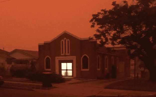 Beobachtung eines hell erleuchteten Gebäudes während eines Sonnenuntergangs in einem Wohngebiet, dekorative Fenster und Baum im Vordergrund, ruhige und friedliche Atmosphäre.