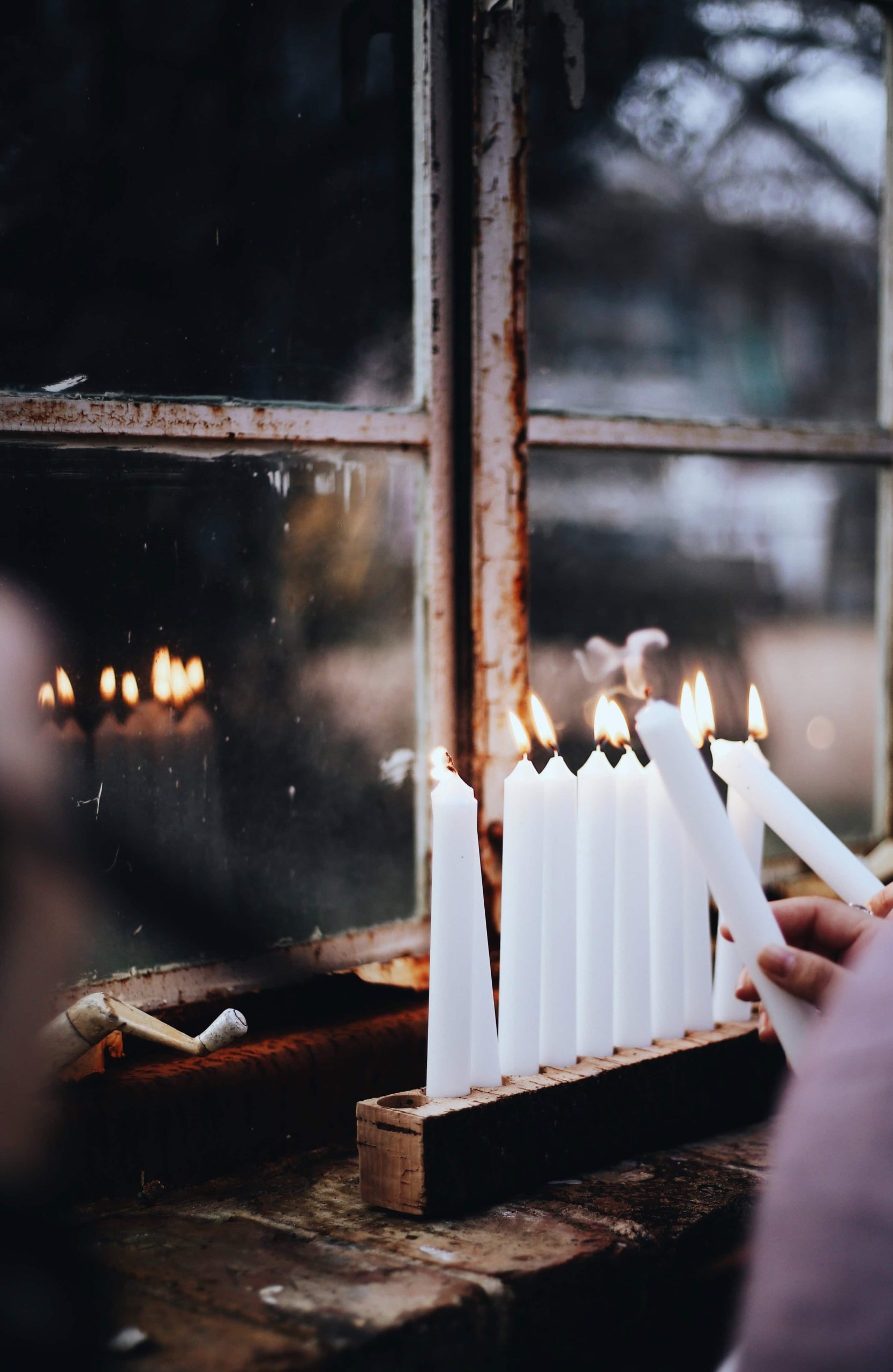 1. Kerzen werden an einem Holzhalter neben einem alten, rustikalen Fenster in der Adventszeit entzündet.