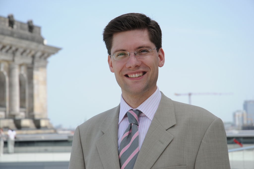 1. Junges professionelles Business-Foto eines Mannes in Anzug mit Brille vor moderner Stadt- und Bauwerkskulisse, urbanes Umfeld, Business-Lifestyle, Frühling.