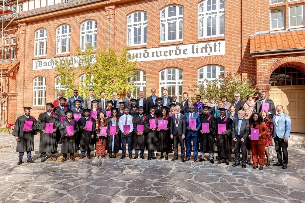 Absolventenfeier vor einem historischen roten Backsteingebäude, viele in Rektoratsrobe mit Urkunden, feierliches Event, Bildung, Abschluss, Hochschule, Erfolg, Team.