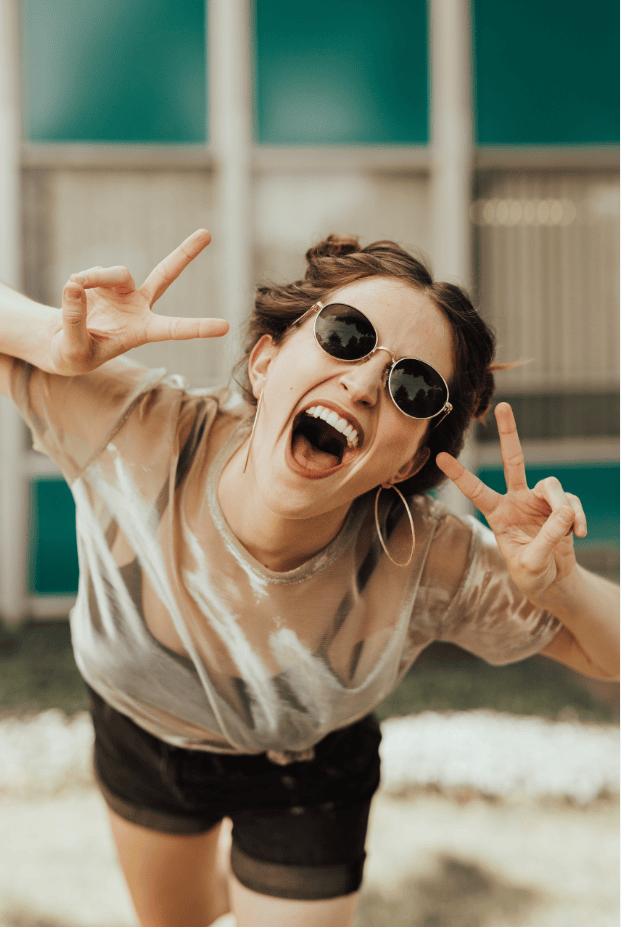 Fröhliche junge Frau mit Sonnenbrille macht Peace-Zeichen, kreativ, Lifestyle, Spaß, Sommer, outdoor, modische Kleidung, positive Stimmung, Sommerfest, Freizeit, Lifestyle-Bilder.