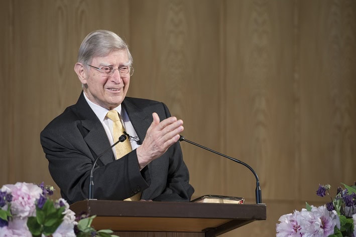 Hochwertiges Bild eines älteren Mannes, der auf einer Bühne hält, theologisch spricht, mit Blumen dekoriert, ideal für christliche Verlage, Prediger oder spirituelle Veranstaltungen.