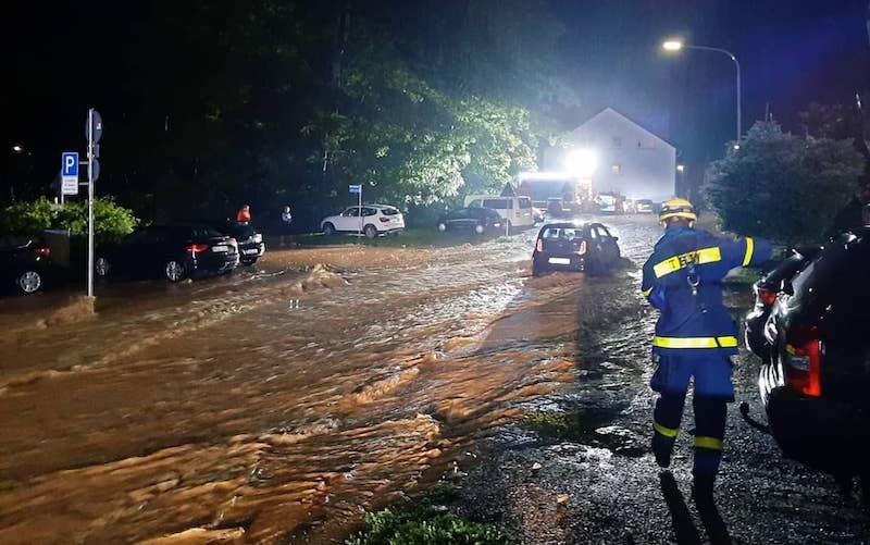 1. Feuerwehrmann bei Hochwasser in einer parkenden Parklücke, Wasser staut sich auf der Straße, Nachtaufnahme, Einsatz bei extremen Wetterbedingungen, Rettungseinsatz, Katastrophenschutz.
