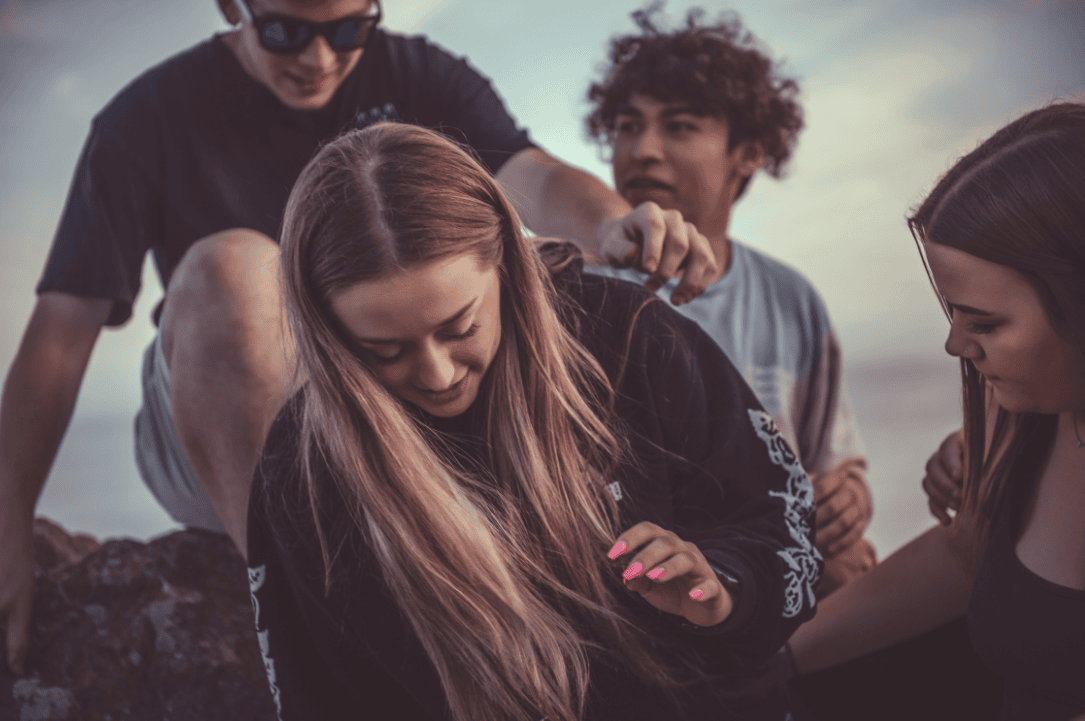 Abenteuerliche Szene mit Freunden am Strand bei Sonnenuntergang, freundschaftliche Unterstützung und Gemeinschaftsgefühl im Fokus, ideal für für Teens, Freizeit, Gemeinschaft, gemeinsam aktiv.