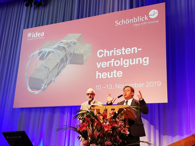 1. Alternativer Text: Christliche Botschaft bei einer Veranstaltung mit einem Kreuz und einer israelischen Flagge, Fokus auf Christenverfolgung, November 2019.