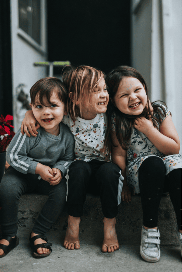 Fröhliche Kinder sitzen zusammen, lachen und genießen sonnigen Tag im Garten, passend für Familien- und Kinderbücher, die beim Advent-Verlag erhältlich sind.