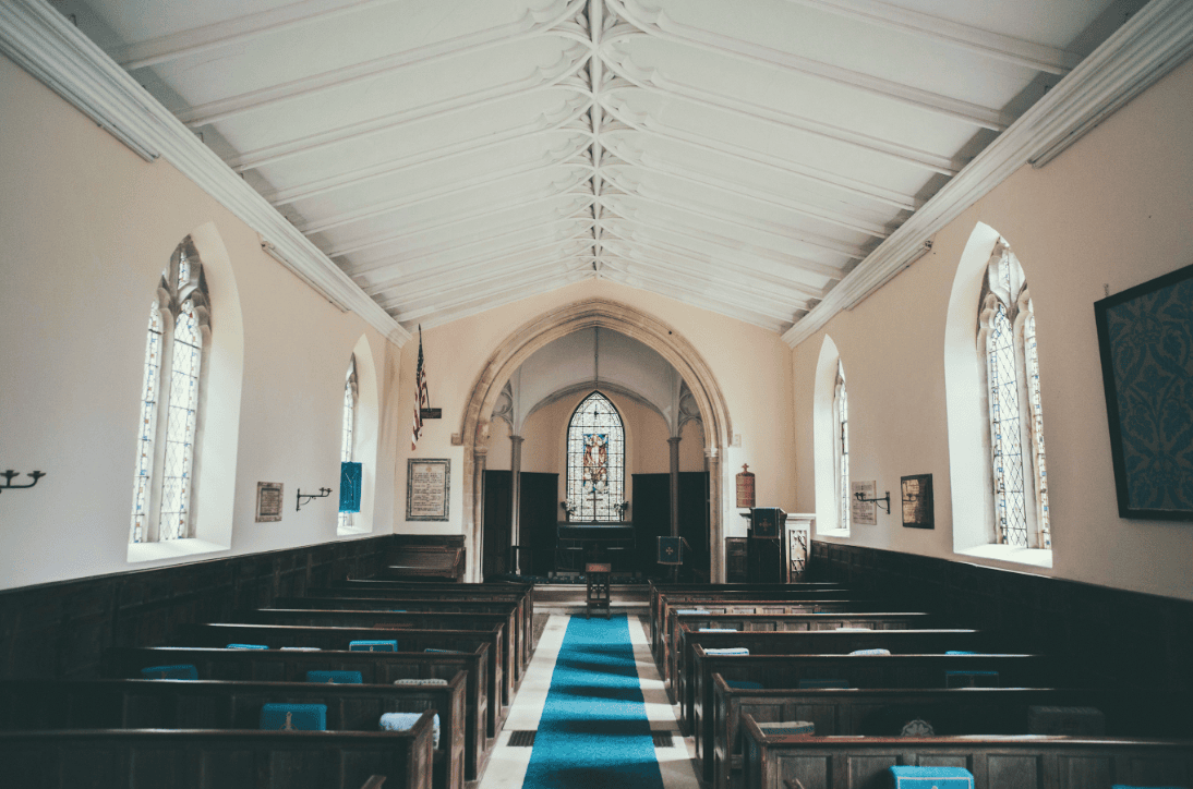 Ruhiger Innenraum einer historischen Kirche mit Bänken, bunten Glasfenstern und Altar, ideal für spirituelle Veranstaltungen, Gottesdienste und Gebetsgemeinschaften. Perfekt für religiöse Gemeinschaften und Gottesdienste.