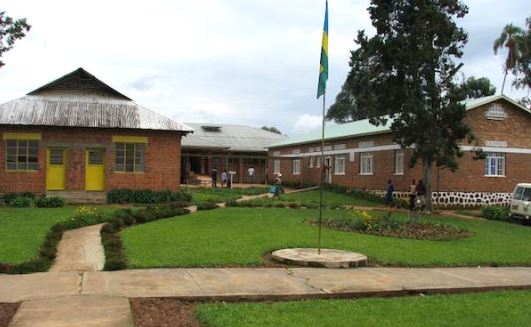 Alter Text: Traditionelle katholische Schule in ugandischer Umgebung mit gepflegtem Hof und Flagge, umgeben von Bäumen und gepflegtem Rasen.