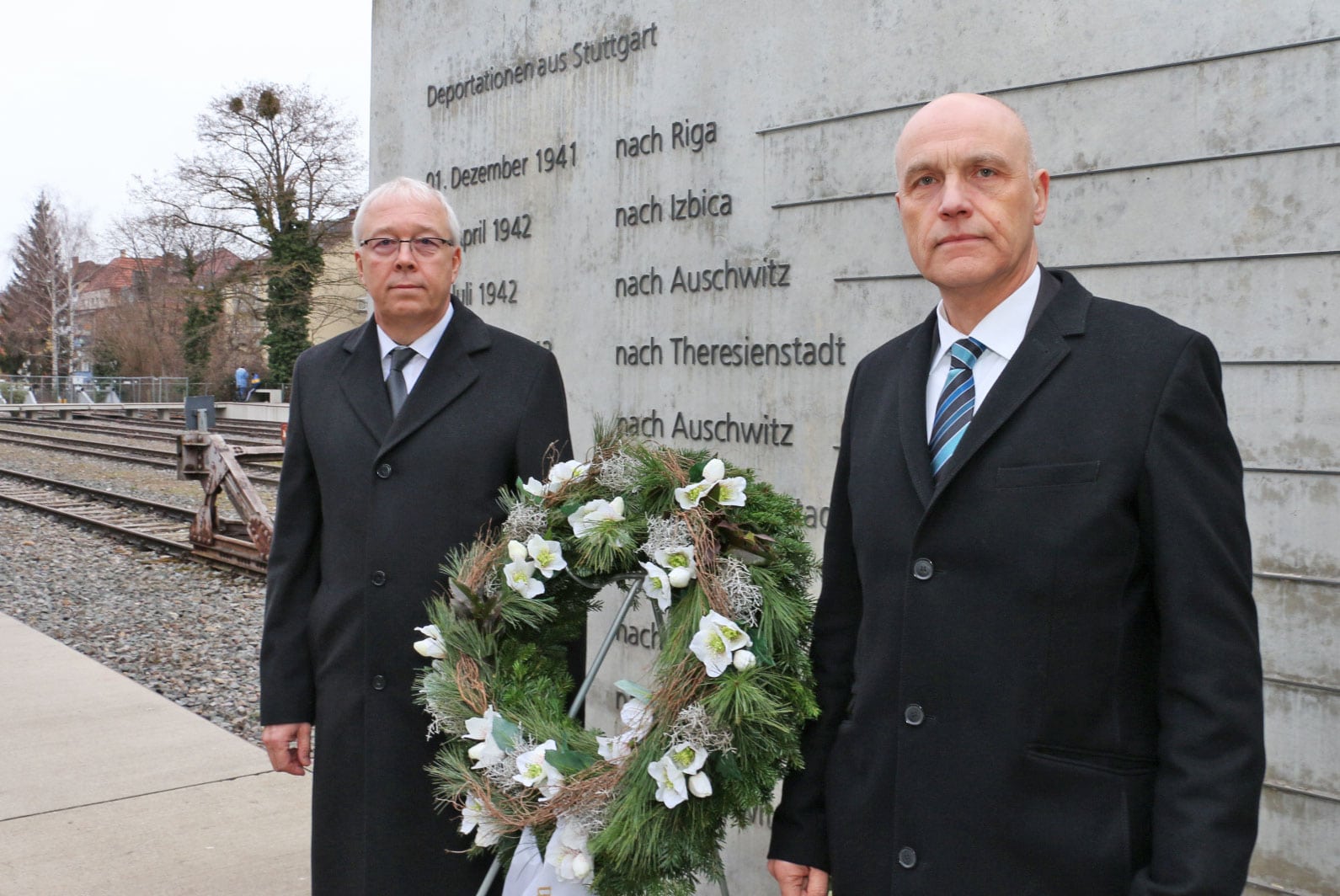1. Gedenkzeremonie am Denkmal für Deportationen aus Stuttgart mit zwei Männern in dunklen Anzügen und Kranz, Erinnerung an historische Ereignisse und Opfer.