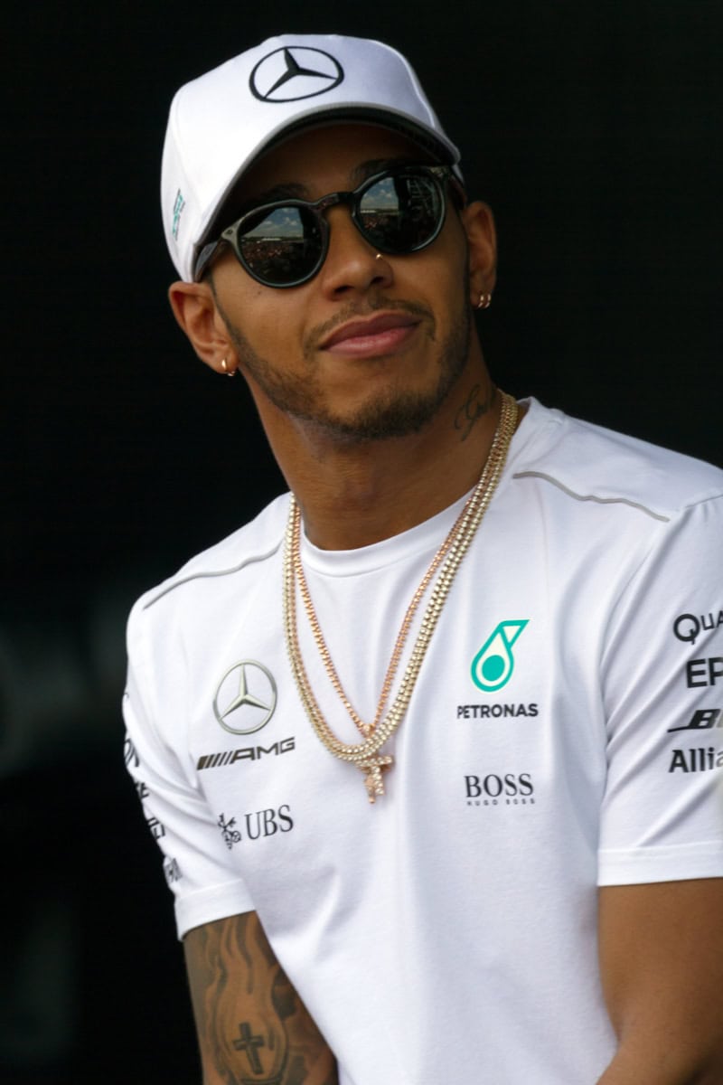 Großer Blick auf einen stilvollen Mann in Mercedes-AMG Petronas Formel 1 Team Kleidung, trägt Sonnenbrille, Kette und Cap, symbolisiert Luxus, Motorsport, und Markenbindung, ideal für Automobil- und Sportfans.