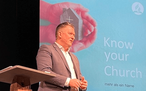 Hände halten ein kleines Kirchenmodell vor einem blauen Hintergrund mit der Aufschrift „Know your Church“.