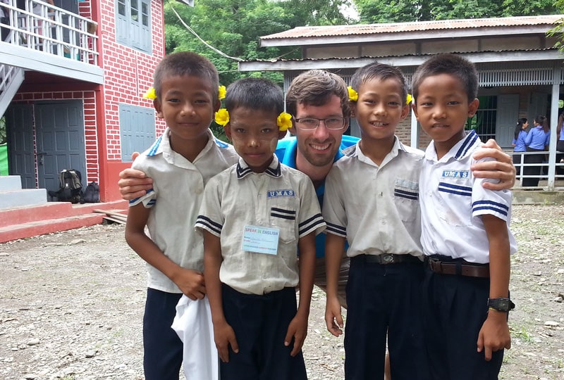 Betreuung eines jungen Mannes mit vier Kindern in Schuluniform aus Nepal vor einem Schulgebäude, für Bildungsprojekte und interkulturelle Austauschprogramme.