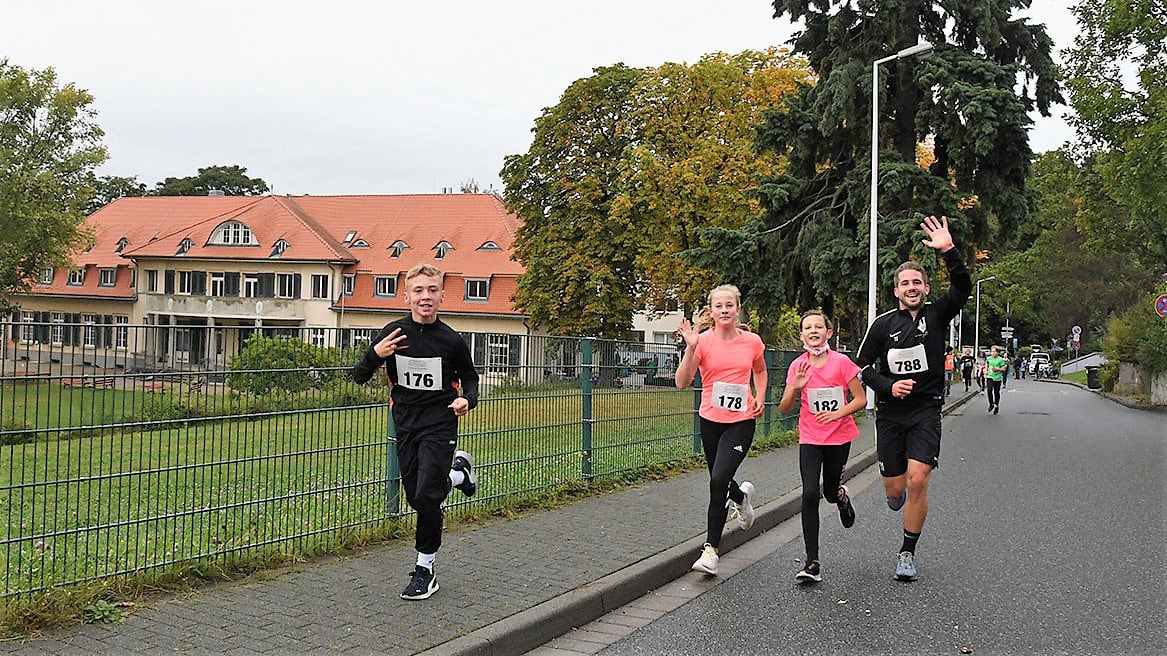 Laufszene beim Gemeinschaftslauf, motivierte Läufer mit Nummern, Kinder und Erwachsene, auf der Straße in einer grünen Vorstadt, bei einem Event des Advent-Verlag in Deutschland.