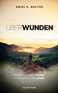 Erwachsener Mann steht auf einem Felsen und blickt auf eine bewaldete Tallandschaft bei Sonnenaufgang, symbolisiert spirituelles Wachstum und Überwindung von Wunden.