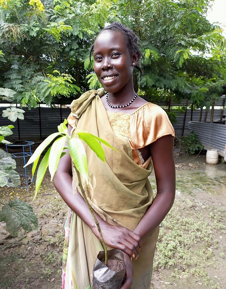 Blinde Frau in traditioneller Kleidung pflanzt Baum in einem Garten - Nachhaltigkeit, Umwelt, Baumpflanzung, Entwicklungshilfe, Frauen empowerment.