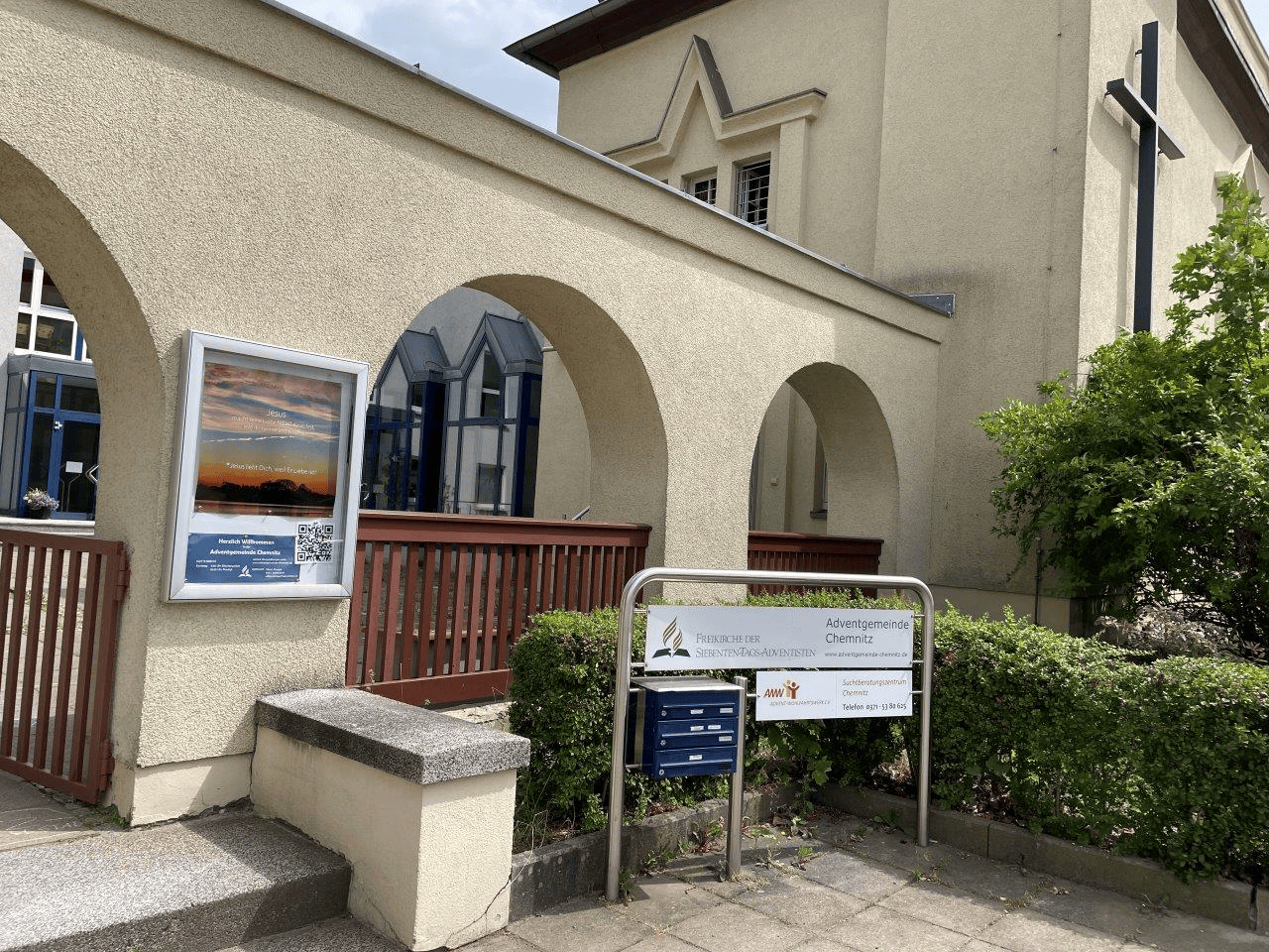Advent-Verlag Kirche Chemnitz Außenansicht mit Kreuz und begrüntem Bereich.