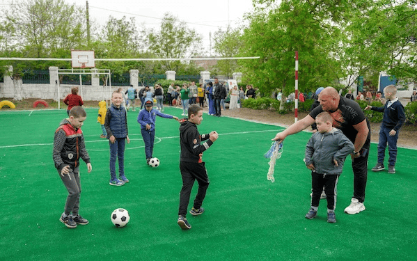 Kinderspiele auf dem Schulhof mit Fußball und Wasseraktivitäten, Spaß und Bewegung, outdoor, Gemeinschaft, Schüler und Lehrer bei einem sportlichen Schulveranstaltung.