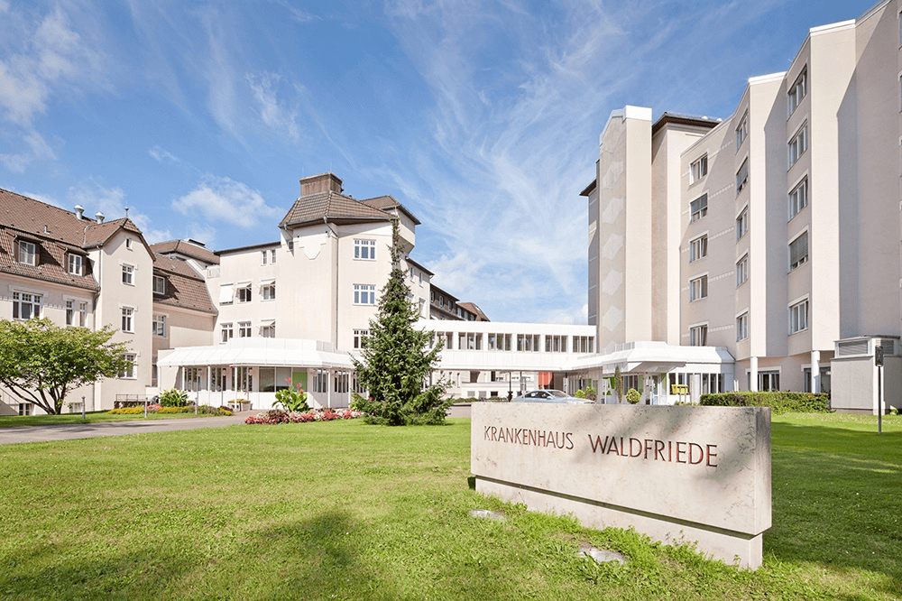 Hohes Gebäude des Krankenhauses Waldfried mit grünem Garten und blauer Himmel, modern gebautes Pflege- und Krankenhaus, angenehme Außenansicht für Patienten und Besucher, Standort in Deutschland.