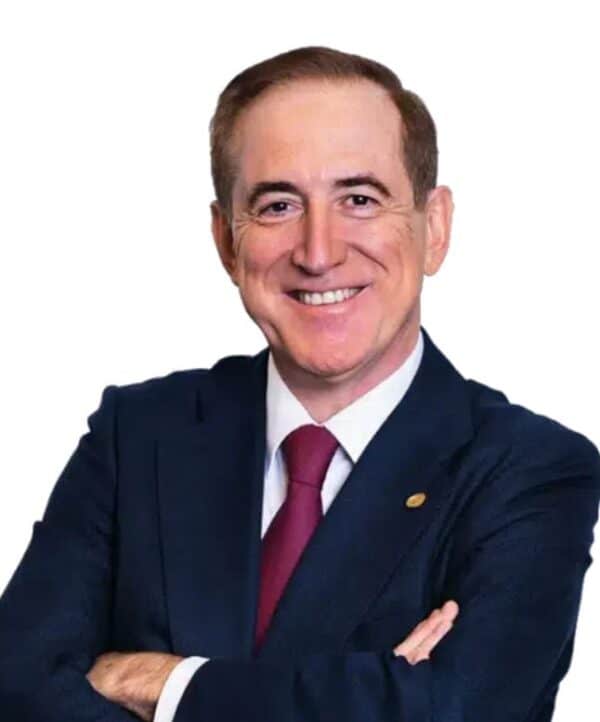 Smiling man in a dark suit with a red tie, arms crossed, against a white background.