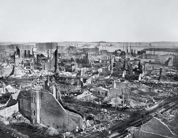 Black-and-white panoramic photograph showing destroyed buildings and rubble following the Great Boston Fire of 1872, with Boston Harbor in the background.