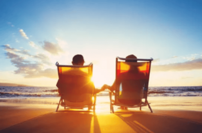 two people sitting in chairs on beach at sunset