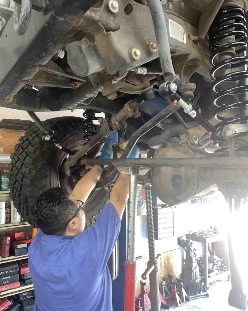 Mechanic inspecting vehicle suspension undercarriage in shop.