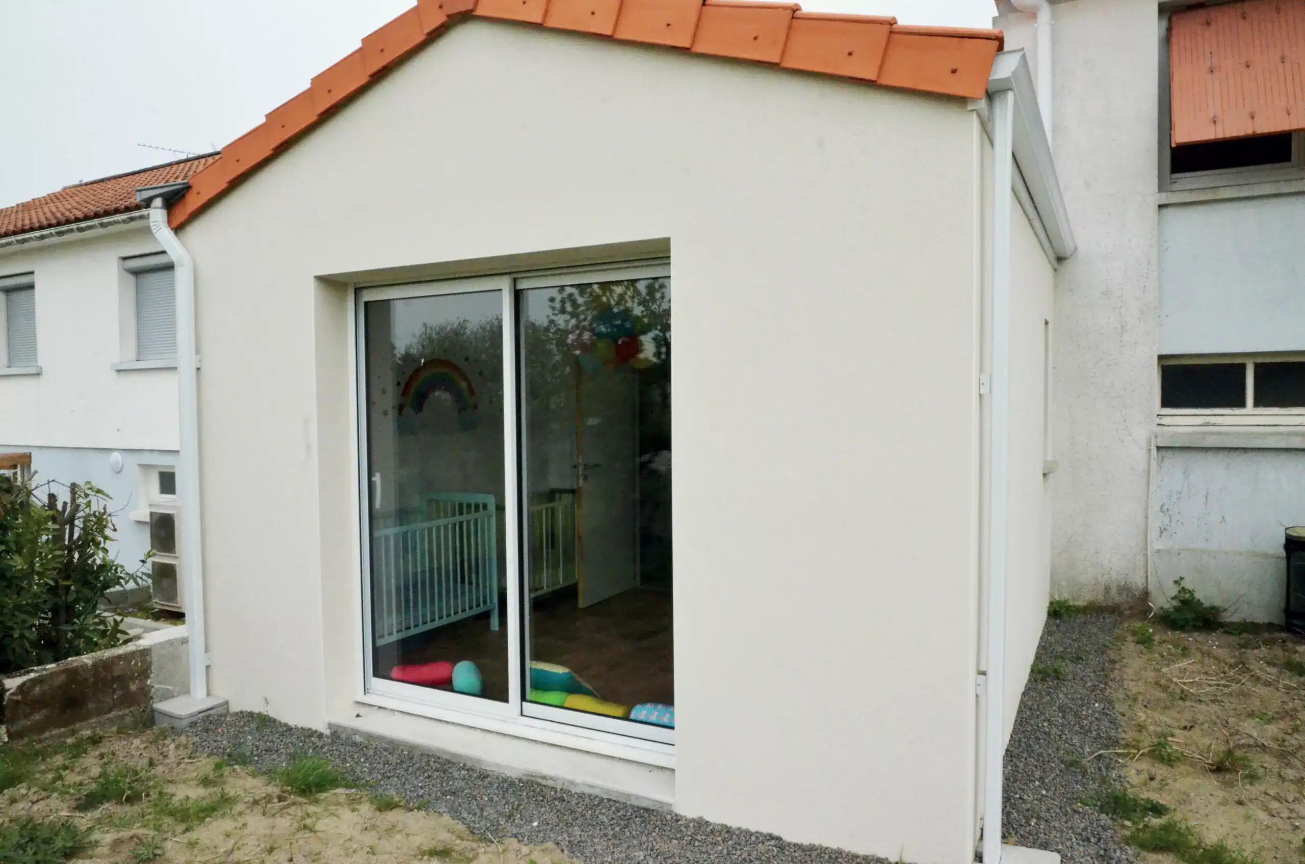 Une extension moderne avec une finition d'enduit clair, agrémentée d'une toiture inclinée en tuiles, intégrant de grandes baies vitrées pour maximiser la luminosité naturelle.