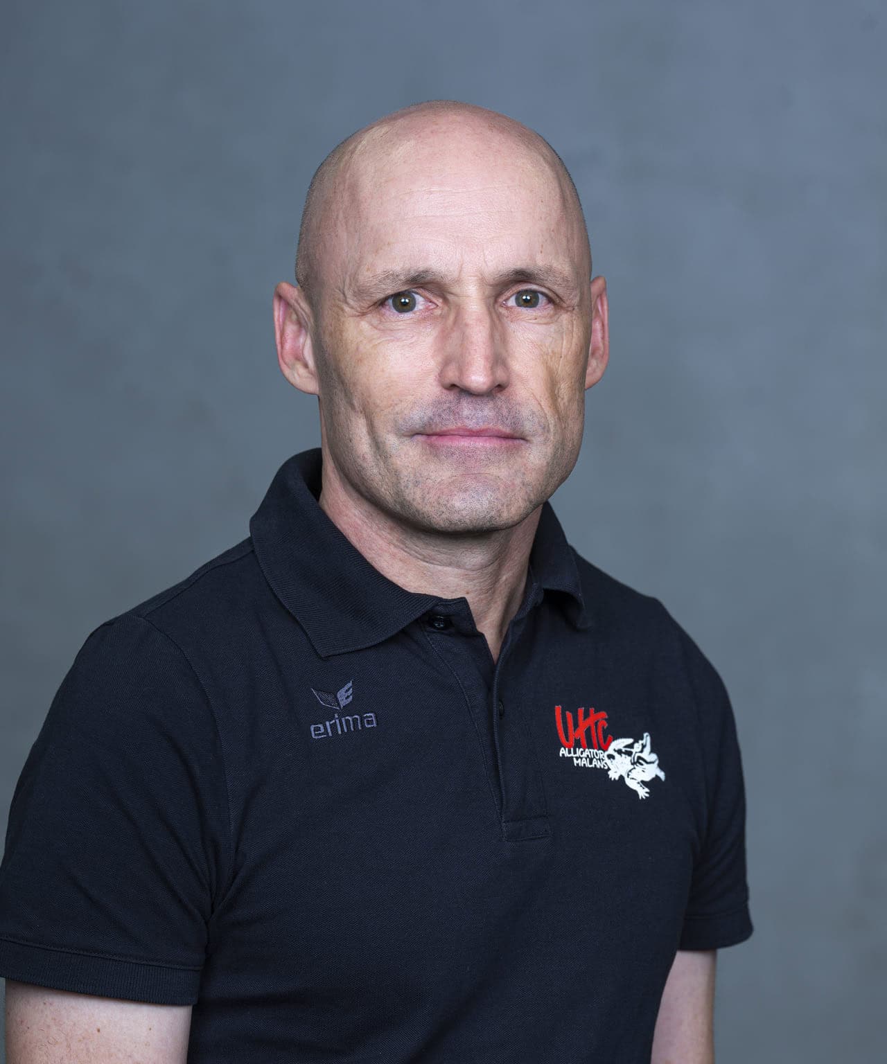 Fotografie eines Mannes trägt ein UHC Alligator Malans Logo auf seinem schwarzen Polo-Shirt. Er ist im professionellen Umfeld, wahrscheinlich im Zusammenhang mit dem Eishockey-Team Alligator Malans.
