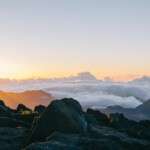 Cumbre montañosa al amanecer con nubes y cielo despejado en un paisaje natural.
