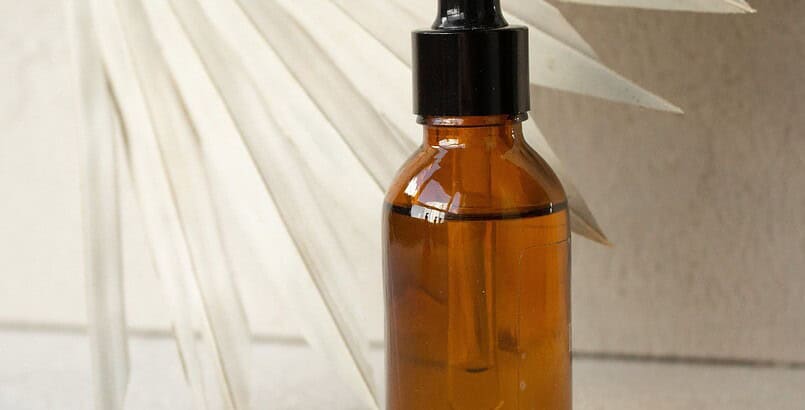 Flacon de cosmétique en verre ambré sans étiquette, posé devant une feuille de palme séchée